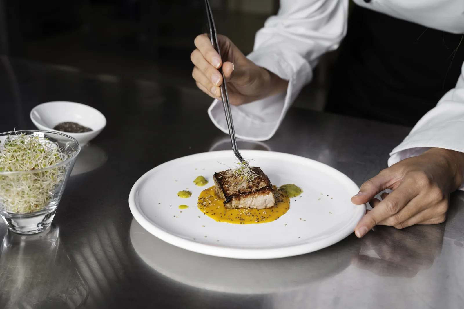 A kitchen staff plating a dish on a clean plate during peak hours at the restaurant.
